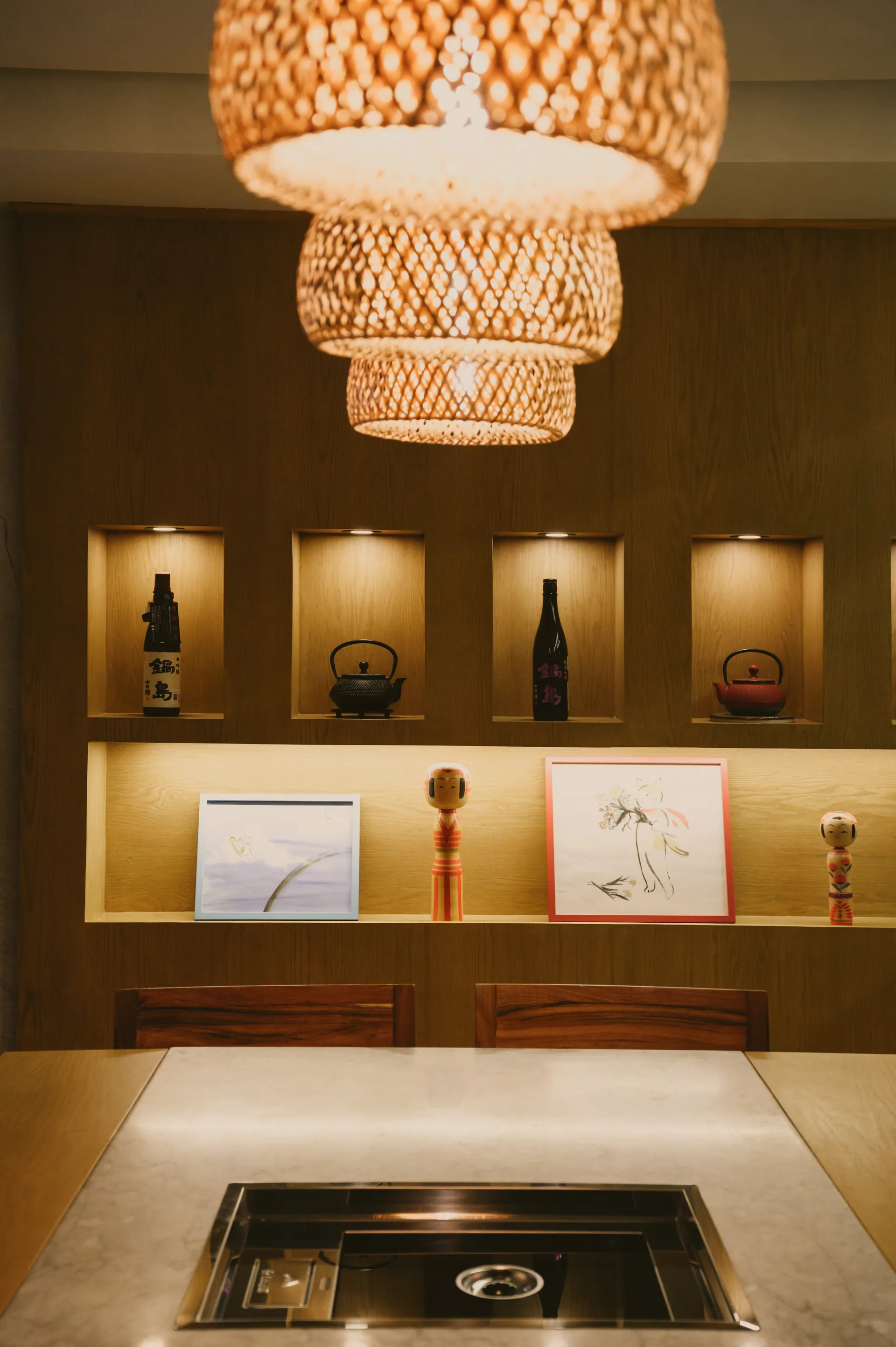 Ambiente intimo en Torobi Polanco: lamparas tejidas, botellas de sake iluminadas y kokeshis japonesas