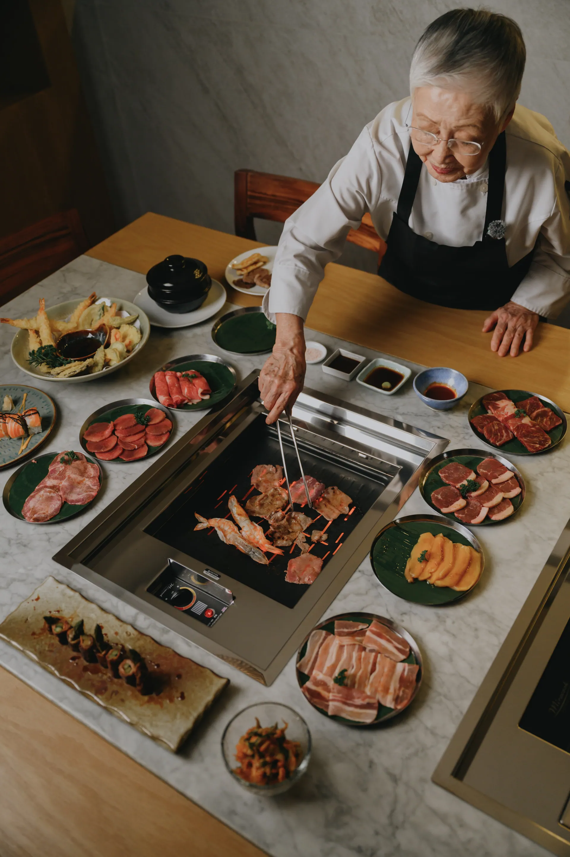 Chef Kazu Kumoto en la mesa de yakiniku de Torobi con cortes premium y mariscos para maridar con sake